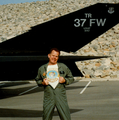 Leo in front of his F117, 
holding open his flight suit to show a GD shirt